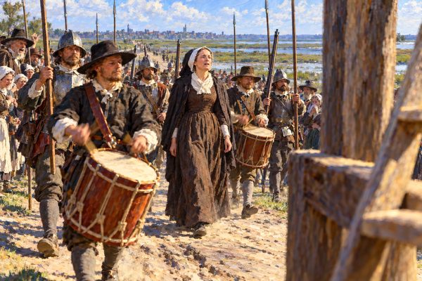 A calm woman in a plain brown dress and white linen cap walks up a dusty marsh road between two drummers and soldiers carrying tall pikes, toward the blurred timber post of a gallows at the right edge of the picture.