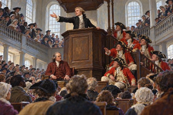 In a tall packed meeting house, a young man in a black coat stands in a high pulpit with one arm flung out, while scarlet-coated officers on the pulpit stairs lean forward hissing and a plainly dressed man sits below facing them.